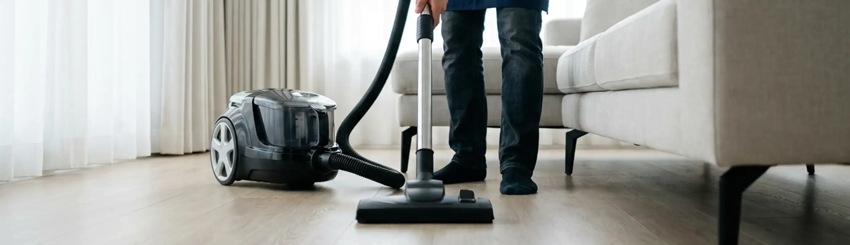 Professional house cleaner vacuuming a living room floor with a canister vacuum cleaner, Savannah, GA.