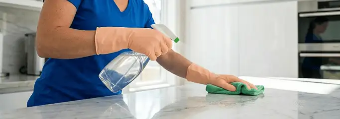Maid service worker spraying and wiping a kitchen countertop with a microfiber cloth for sanitizing, Savannah, GA.