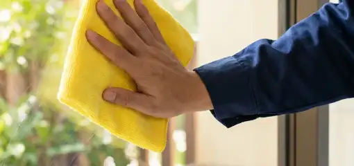 House cleaner wiping a glass window with a yellow microfiber cloth for streak-free cleaning, Savannah, GA.